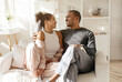 © Anastasiya - Sweet loving african american couple sitting on couch at home. Handsome eastern husband hugging his beautiful wife, looking at copy space together, smiling, cozy living room interior. High quality
