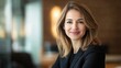 © sirisakboakaew - Professional woman in business attire, working on a project, looking directly at the camera with a warm smile in a modern office