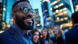 © DKPhoto - A sharply dressed man with glasses smiles confidently amidst a blurred cityscape at night, projecting an aura of success, optimism, and modern urban life.