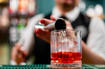 Wall Mural - A bartender pours a drink into a textured glass, with a blurred background. The close-up shot captures the intricate details of the glass and the liquid, creating a dynamic and inviting scene