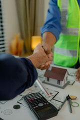 Poster - engineer and architect are shaking hands to celebrate because they just finished big construction project, two engineers do handshake after the meeting, blueprint is on the desk