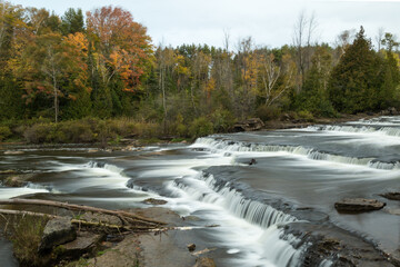 Wall Mural - Subdued fall colors beside a tiered cascade waterfall. A long exposure autumn waterfall scenery.