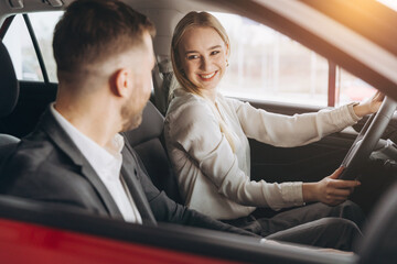 Wall Mural - Competent car dealer showing female customer interior of luxury auto. Caucasian man and woman sitting inside and talking. Concept of selling and purchase.