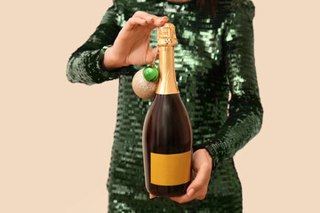 Woman in green dress holding bottle of champagne with Christmas balls on beige background