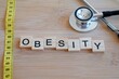 © Inspiraciones - OBESITY. Wooden letters with tape measure and stethoscope.