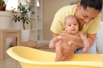 Wall Mural - Beautiful young happy mother with cute little baby bathing at home