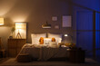© Pixel-Shot - Interior of dark bedroom with glowing lamps, laptop and books on bed at night