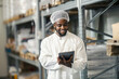 © Dusan Petkovic - Black storage manager in sterile uniform working on checklist and smiling at tablet at warehouse.