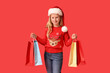 © Pixel-Shot - Cute girl in Santa hat with shopping bags on red background. Christmas celebration