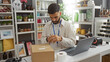 © Krakenimages.com - Young man with beard using mobile in home decor store, surrounded by shelves filled with various decorative items, scanning product at counter, laptop and barcode scanner visible.