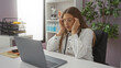 © Krakenimages.com - Woman stressed at clinic desk wearing glasses showing fatigue with laptop in hospital room surrounded by medical equipment and documents seeking a moment of relief indoors