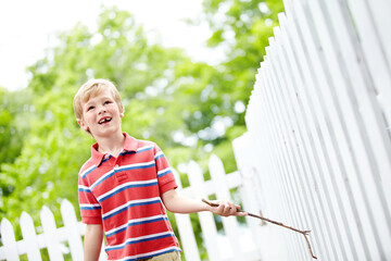 Smile, stick and playful with kid and picket fence for fun, break and summer vacation. Happiness, explore and childhood development with young boy in backyard of home for holiday and outdoors