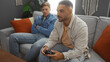 © Krakenimages.com - Friends playing video game in cozy living room with plants and colorful pillows, focused and relaxed, emphasizing indoor bonding between men in casual outfits, capturing modern apartment vibe