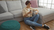 © Krakenimages.com - A beautiful young woman with short hair in a home living room, sitting on the floor by a grey couch, looking at her phone and holding a white bottle.