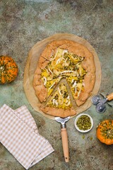 Wall Mural - Savory gluten free galette with pumpkin, brie cheese and pumpkin seeds on buckwheat crust on green concrete background. Gluten free recipes. Pumpkin baking.