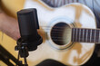 © Studio Marmellata - A focused image of a microphone set up next to an acoustic guitar, capturing the details of the equipment in a home recording environment, ideal for producing high-quality sound indoors.