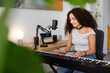 © Studio Marmellata - young woman is focused on her keyboard practice in a home studio, sitting by a microphone in a creative and professional setup that highlights her musical dedication and skill.