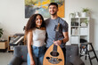 © Studio Marmellata - man holds an oud while standing beside a smiling woman in a contemporary living room, with a colorful painting and musical equipment creating a vibrant and friendly setting for creativity.