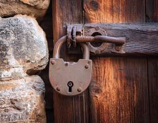 close up view of a rusty padlock on weathered vintage wooden door of an abandoned stone house