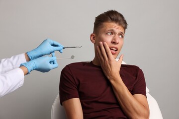 Wall Mural - Dental phobia. Dentist working with scared man on grey background, closeup