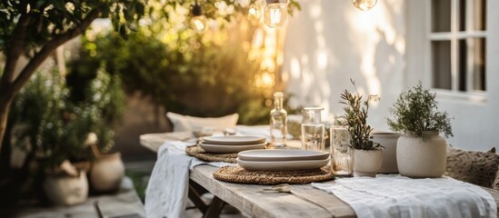 Rustic wooden table set for outdoor dining with white linens, two plates, and greenery in pots.