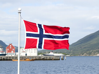 Norwegian flag waving proudly beside a scenic fjord on a clear day with mountains in the background