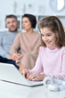 © aletia2011 - Cheerful little girl using a laptop at home with her parents in the background.