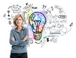 © ImageFlow - Woman standing with arms crossed, colorful lightbulb and business icons in background. White backdrop. Concept of idea and planning