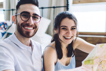 Excited hipster couple having fun and reviewing map while sitting on floor at home