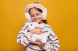 © sementsova321 - Smiling female child receiving stuffed dog as present embracing it with closed eyes and charming smile feeling happy while playing with toy indoors isolated over yellow background