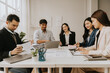 © Kritdanai - Teamwork Makes the Dream Work: A diverse group of business professionals collaborates around a table, engaged in a productive meeting, showcasing their synergy and dedication.