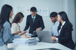 © Kritdanai - Business Meeting in Progress: Diverse team of professionals collaborating in a modern office setting, engaged in a productive discussion around a table. Their focus, energy, and teamwork are palpable.