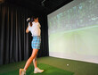 © Nadzeya - A golfer in a stylish outfit swings a club while focusing on a virtual screen displaying a lush green course concept