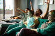 © Marko Geber - Family cheering while watching tv at home on the couch