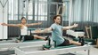 © InfiniteFlow - Two clients performing synchronized arm extensions on Pilates reformer machines. Happy pilates partner seated twist on the reformer for enhancing flexibility and building balance, control. Habituate.