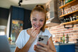 © Geber86 - Happy young woman using smartphone in kitchen