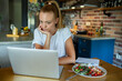 © Geber86 - Woman using laptop on kitchen table while eating healthy meal