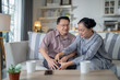 © ultramansk - An elderly couple sits in their living room. The man holds his knee, appearing to be in discomfort, while his partner offers support. The image conveys care, concern, and the bond between the couple.