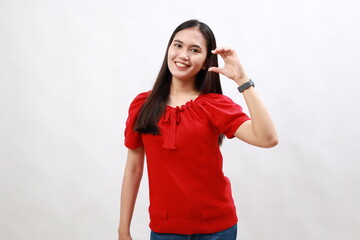 Wall Mural - Young asian woman in red smiling and confident gesturing with hand doing small size sign with fingers looking and the camera. measure concept.