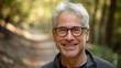 © Tom - A smiling older Caucasian man with glasses on a forest path, showcasing a warm and inviting demeanor amidst vibrant autumn foliage.