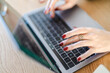 © Studio Marmellata - Close-up of a woman's hands with red nails typing on a laptop keyboard