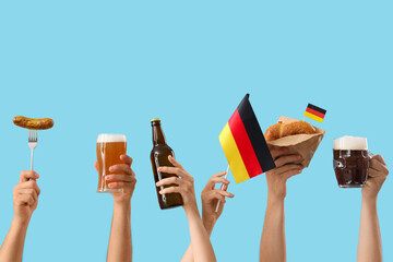 Wall Mural - Many hands with glasses of cold beer, Germany flags and traditional snacks on blue background. Octoberfest celebration