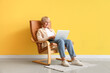 © Pixel-Shot - Old woman with laptop sitting in armchair near yellow wall