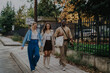 © qunica.com - Three friends are joyfully walking together on a sidewalk, enjoying a leisurely day amidst urban greenery and pleasant weather.