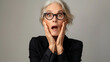 © CybStars - Surprised senior woman with silver hair and round glasses, hands on cheeks, wide-eyed expression of shock in a studio setting, conveying strong emotion and curiosity