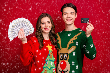 Portrait of two positive people hand hold showing plastic debit card usd dollar banknotes bills isolated on red color background