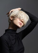 © SHOTPRIME STUDIO - Stylish young woman with short blonde hair posing against a gray backdrop, showcasing modern fashion and confidence. Portrait and beauty concept.