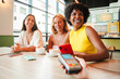 © Jose Calsina - three diverse happy young women friends smiling while making contactless mobile payment with smartphone and credit card terminal at modern cafe during coffee meeting time together
