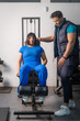 © Guillermo Spelucin - Personal trainer guiding client exercising on gym machine