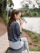 © SHOTPRIME STUDIO - Thoughtful young woman sitting by the river, enjoying her vape while contemplating life Peaceful outdoor setting with nature and calm waters